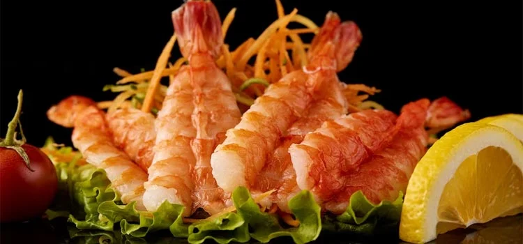 cooked shrimp with lemon and tomato in a black background