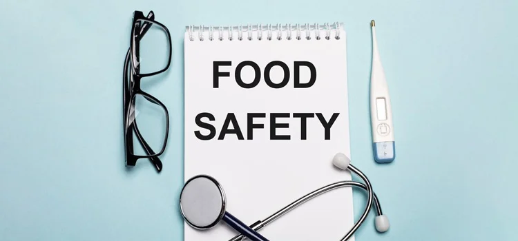 food safety is written on a white notebook with glasses, thermometer and stethoscope