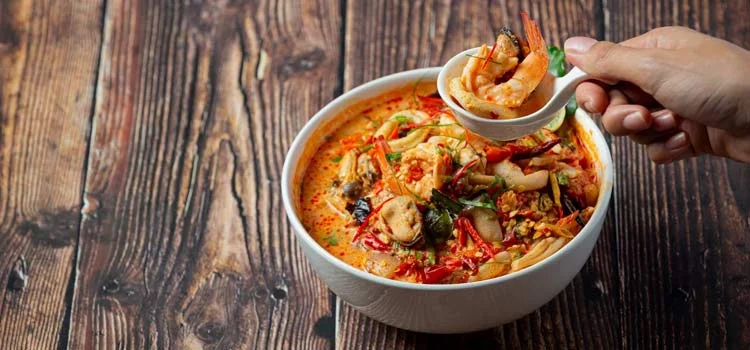 a person is eating Spicy prawn soup served in a white bowl