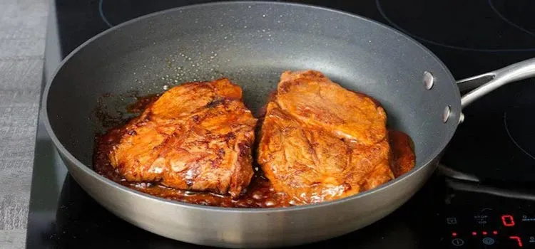 pork steaks are being fried with sauce in a frying pan