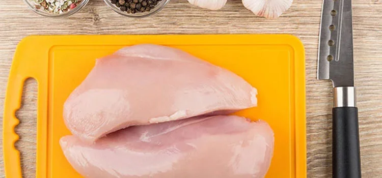 yellow chopping board with raw chicken and a knife