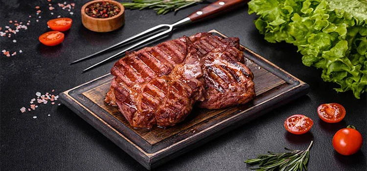 Grilled beef steak served on wooden board with vegetables and herbs