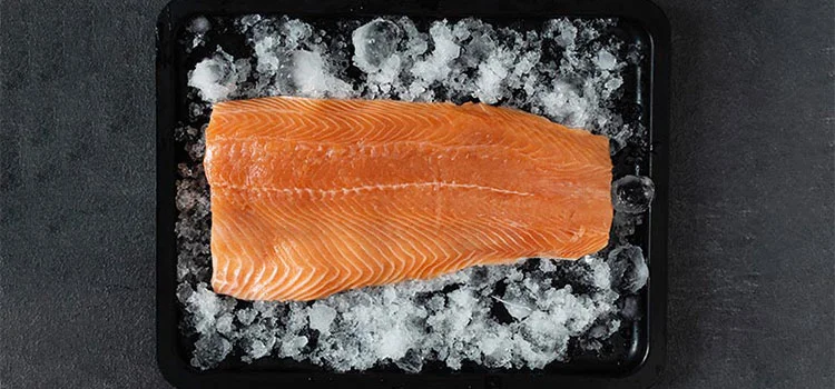 A raw salmon fish fillet in ice in a black tray 