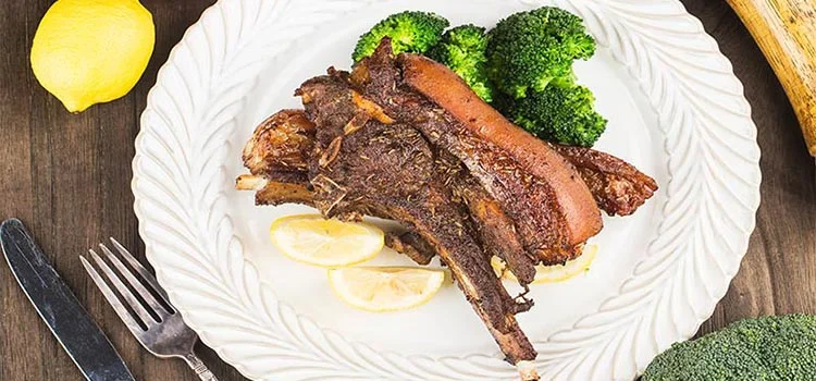Delicious roast lamb chop served on a white plate with broccoli and lemon 