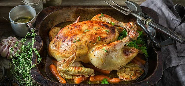 Tasty whole chicken grilled served with thyme and carrots in a pan