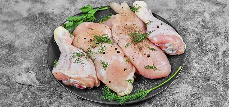 Raw chicken meat slices on a black plate with chopped herbs and black pepper