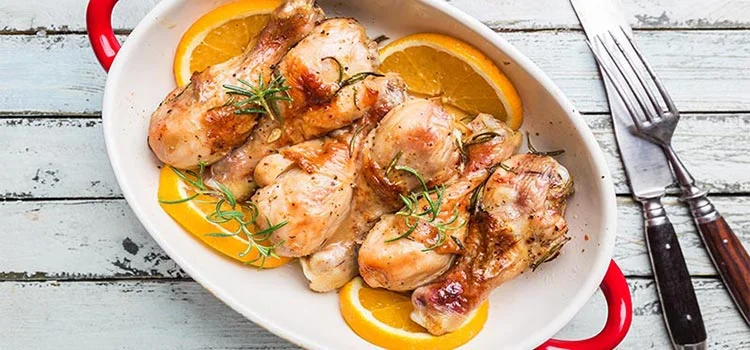 Baked chicken drumstick in a dish with orange and rosemary