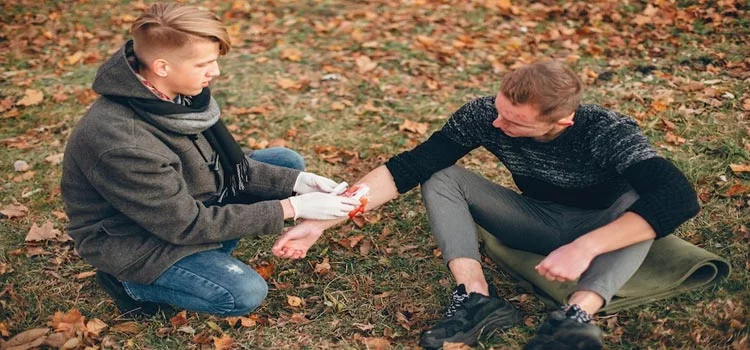 A man Providing first aid to another man with an injured hand in the park 