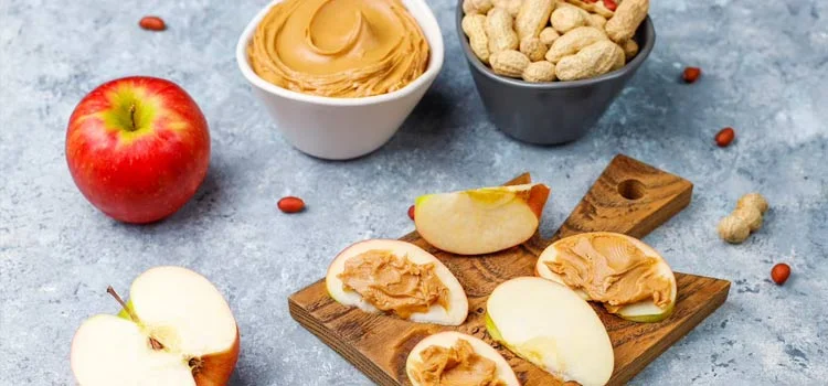 Close-up of peanut butter with peanuts layered on apple slices.