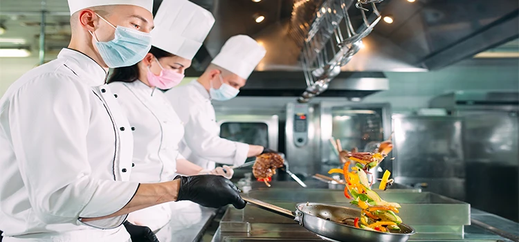 Chefs in protective masks and gloves preparing food in the kitchen of a restaurant.