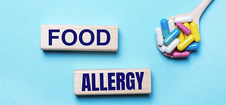  A light blue background, bright multi-coloured pills in a spoon and two wooden blocks with the text food allergy. 