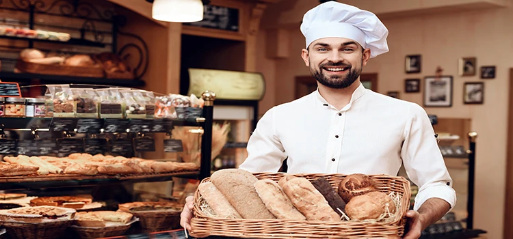 Young bearded man in white cap holding a bucket of baked items.