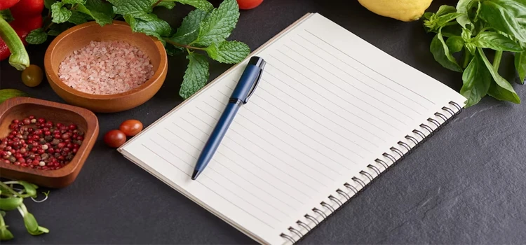 Close-up of notepad and pen surrounded by food items.