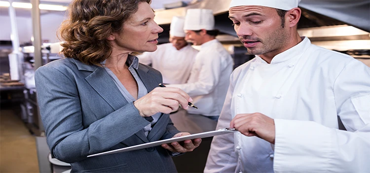 Female restaurant manager writing on clipboard while interacting with head chef.