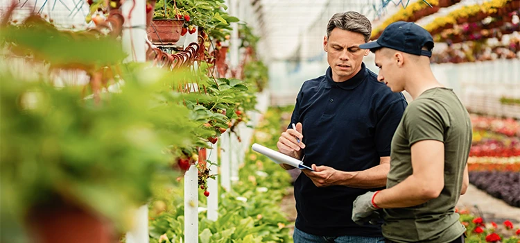 Quality control inspector and worker talking while going through a list of plants in a greenhouse 