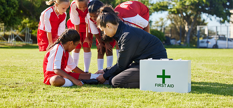 Coach is administering first aid to a young girl with a leg injury in soccer.